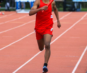 Front view of a runner in a bright red uniform sprints down the track during a relay race.