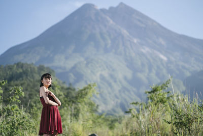 Woman looking away while standing against mountains and sky