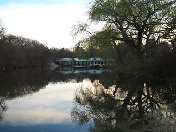 Reflection of trees in lake against houses and sky at dusk