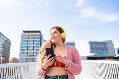 Young woman listening music against sky