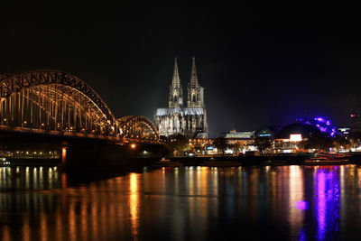 Illuminated bridge over river against buildings at night