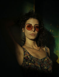 Portrait of young woman wearing sunglasses against wall