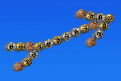 Close-up of bitcoins arranged as arrow symbol against blue background