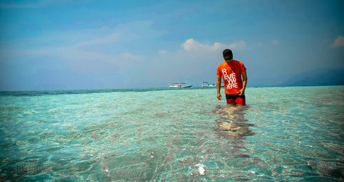 Rear view of man standing in sea against sky