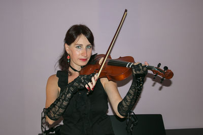 Portrait of beautiful woman playing violin against wall