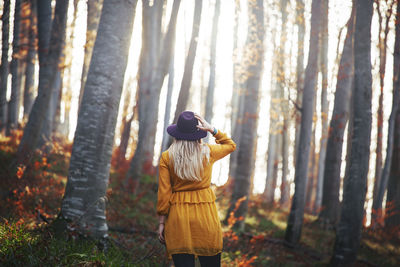 Rear view of woman standing by tree trunk in forest