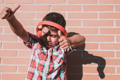 Cheerful boy listening music while standing against wall