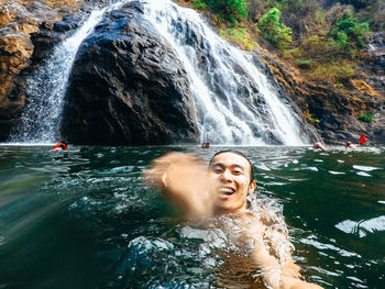 People in river against rock and waterfall