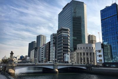 Bridge over river by buildings against sky in city