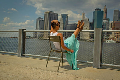 Rear view of woman with railing against sky in city