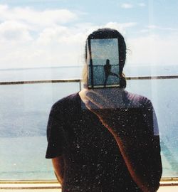 Woman standing against sea seen through glass window