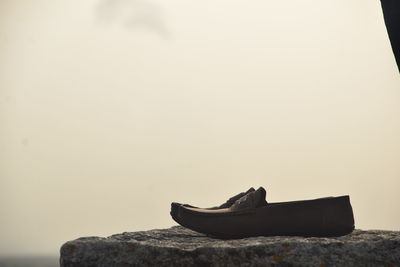 Close-up of shoes on rock against clear sky