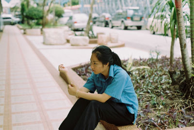 Side view of woman looking away while sitting on footpath