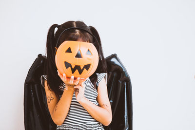 Playful girl covering face with jack o lantern bucket against wall