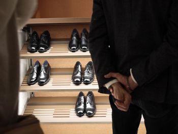 Midsection of man standing with hands behind back against shoes on rack at store