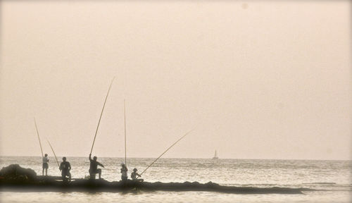 Silhouette people fishing in sea against clear sky