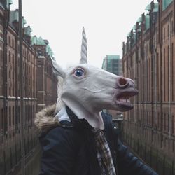 Man wearing unicorn mask amidst buildings