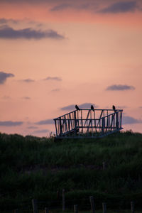 Silhouette metallic structure on field against sky during sunset