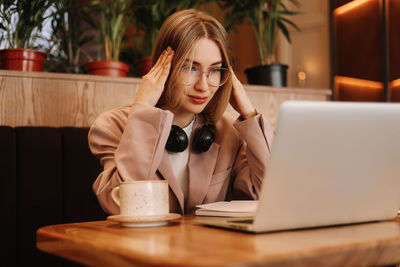 A smiling student wearing glasses and headphones works and studies online using wireless technology