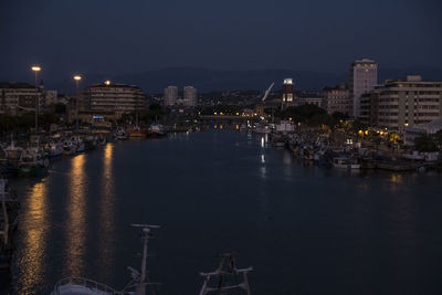 Illuminated buildings by river against sky at night