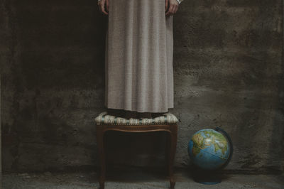 Low section of woman standing on chair against wall at home