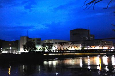 Illuminated city by river against sky at night