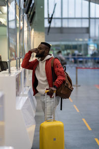 Upset african man standing at check-in counter in airport, being sad about moving away