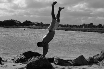 Shirtless young man practicing handstand on rock at beach