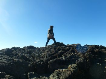 Low angle view of woman standing on rock against sky