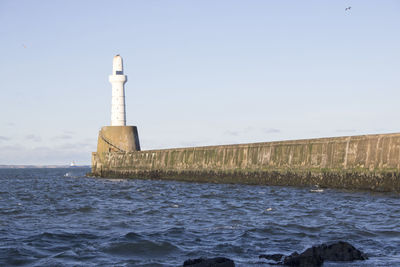 Lighthouse by sea against clear sky