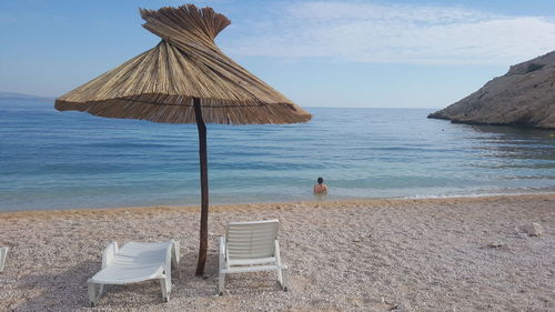 Lounge chars below parasols at beach against sky