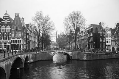 Bridge over river by buildings in city against sky