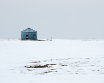 House on frozen field by sea against clear sky