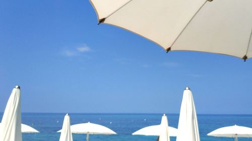 Beach umbrellas by sea against blue sky