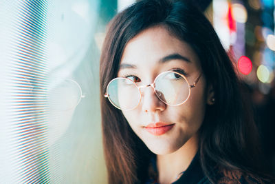 Close-up of young woman standing against illuminated city at night