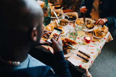 High angle view of young man photographing food in plate while sitting at restaurant during dinner party