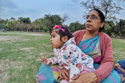 Grandmother and daughter sitting on grass against trees and sky