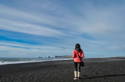 Rear view of woman walking on beach against sky