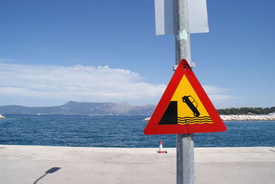 Road sign by sea against sky