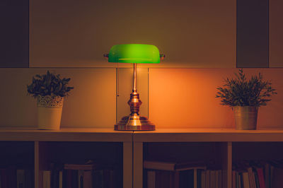 Illuminated electric lamp on table against wall at home