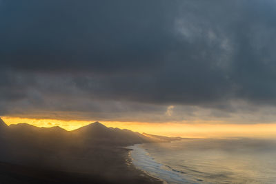 Scenic view of mountains by sea against sky during sunset