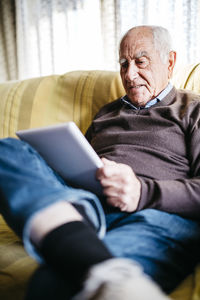 Senior man sitting on couch using tablet