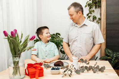 Dad and son prepare a gift for mother's day. decorate the cake with berries. mother's day