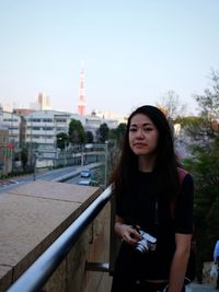 Beautiful young woman standing against sky in city