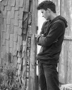 Thoughtful young man with arms crossed standing by old house