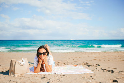 Young woman sitting at beach against sky