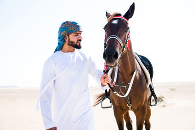 Man wearing traditional clothing standing with horse against clear sky