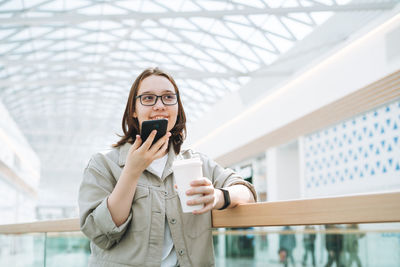Young teenager girl student in glasses using mobile phone sent voice message at shopping mall