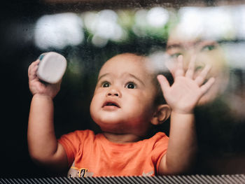 Portrait of cute baby boy looking out of a glass door