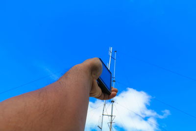 Cropped man holding smart phone by communications tower